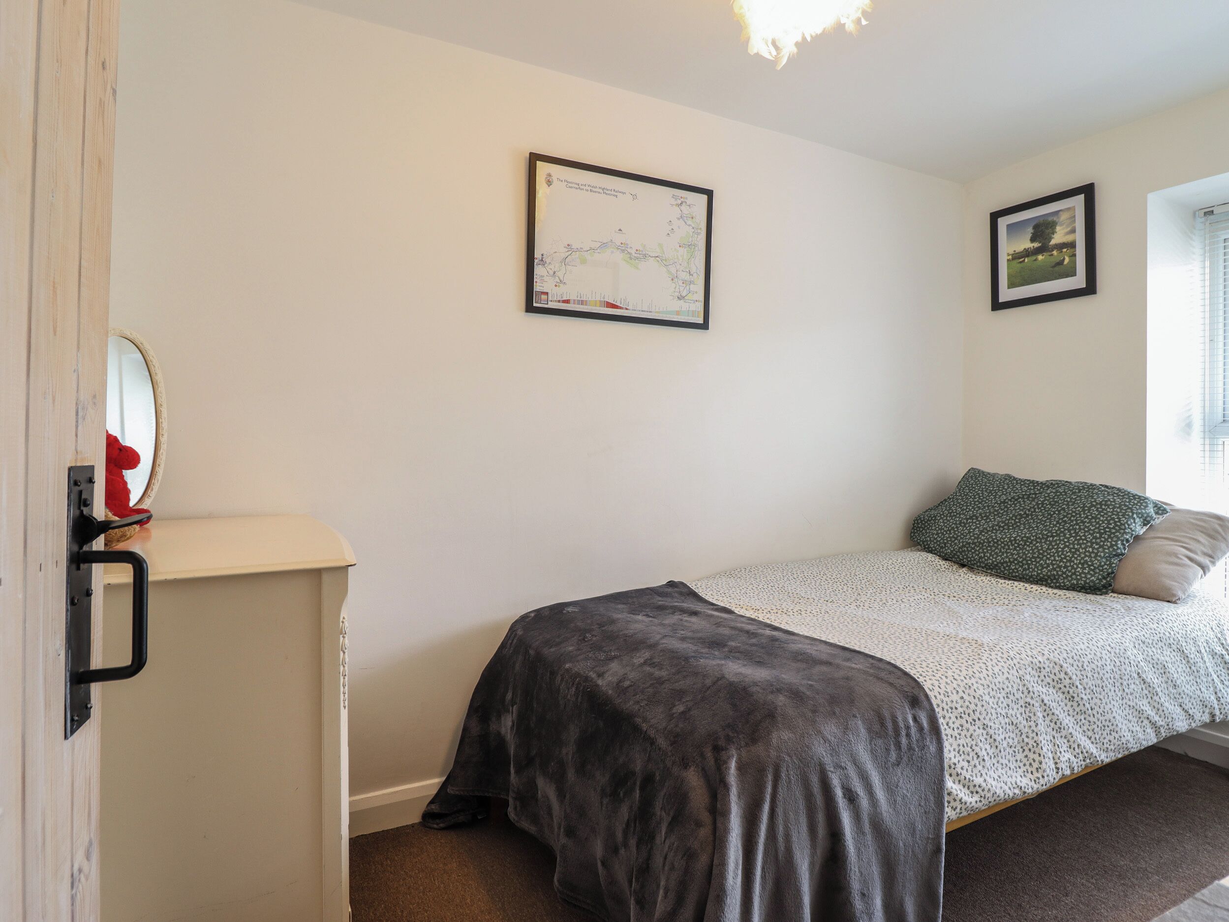 A bedroom with a single bed, a map on the wall, and a window with blinds.