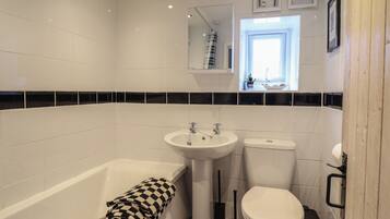 A bathroom with a bathtub, sink, toilet, and a window providing natural light.