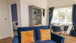 Ein Wohnzimmer mit blauem Sofa, einem Bücherregal und einem Essbereich mit Tisch und Stühlen.