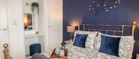 A bedroom with a bed, a nightstand, a lamp, a tray with mugs, and a wall-mounted plant.
