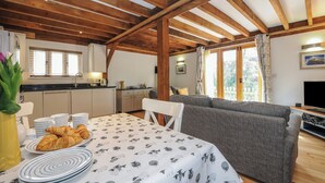 Een knus interieur met een houten plafond, een eettafel met croissantjes, een grijze bank en een televisie.