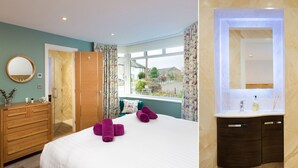 A hotel room with a bed, a wooden dresser, a bathroom with a mirror, and a view of the outside. - Fell View (Keswick)