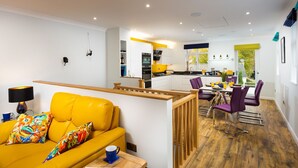 A modern living room with a yellow sofa, a dining area with purple chairs, and a kitchen in the background. - Fell View (Keswick)