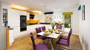 A modern kitchen with white cabinets, a built-in oven, and a dining area with purple chairs and a white table set for four. - Fell View (Keswick)