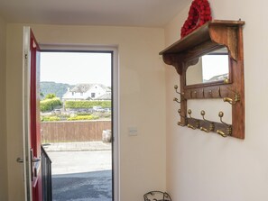 Habitación con perchero de madera, un espejo y una puerta que da al exterior.