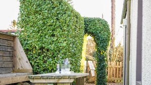 A wooden table with benches in a garden area with a wooden fence and greenery. - Rhum Cottage (Cupar)
