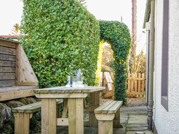 A wooden table with benches in a garden area with a wooden fence and greenery.