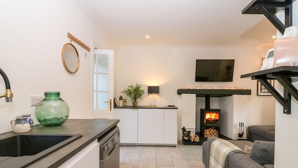 A modern kitchen with a dishwasher, a green vase, and a small table with cups. - Rhum Cottage (Cupar)