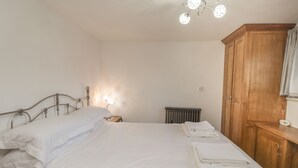 A neatly made bed with white linens, a wooden nightstand with a lamp, a radiator, and a wooden wardrobe.