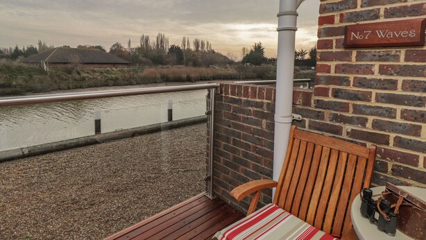 A wooden deck with a striped cushion, a brick wall, and a view of a river.