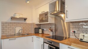 A modern kitchen with white cabinetry, a stainless steel range hood, a microwave, an oven, and a toaster.