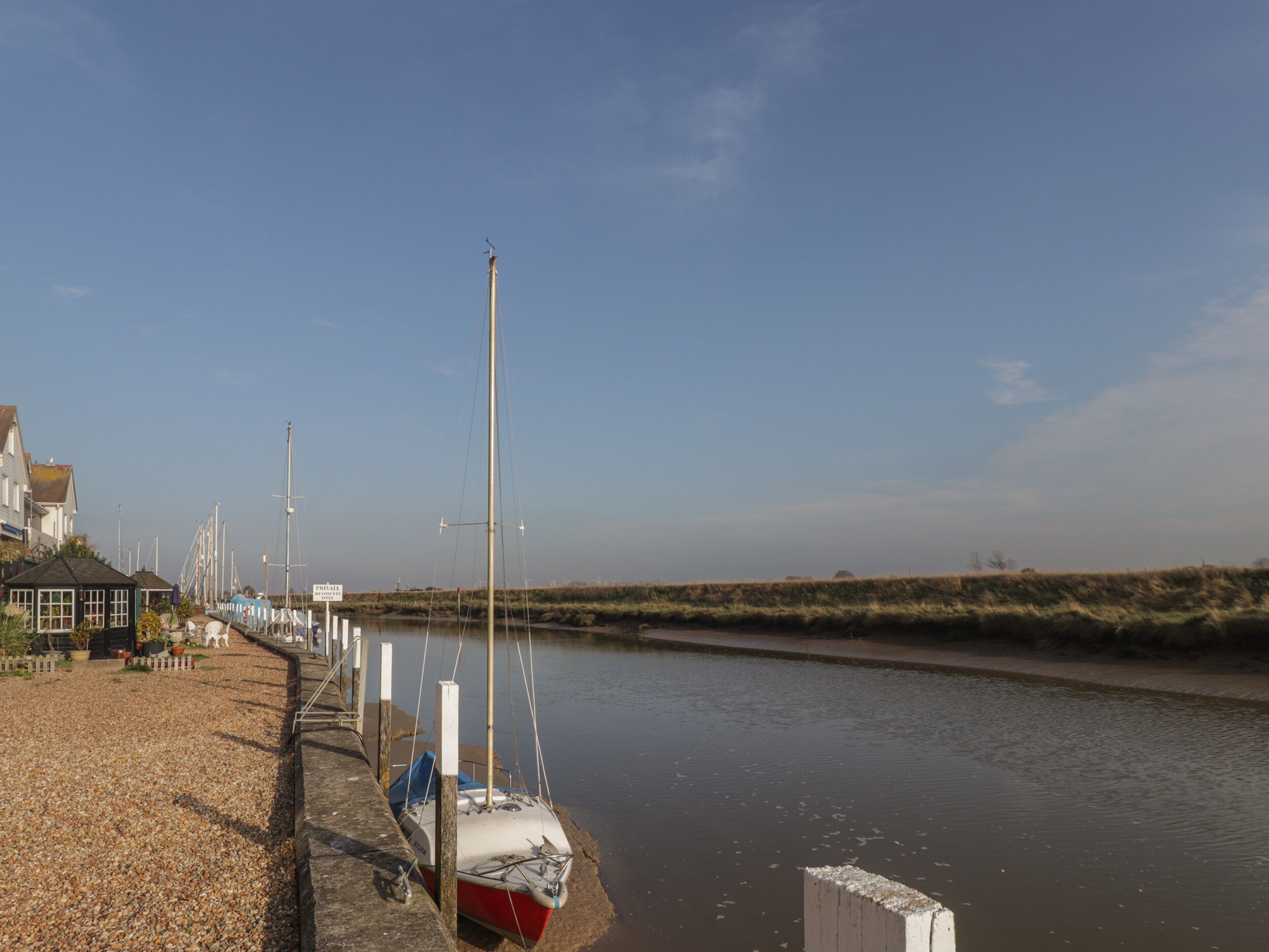 A calm waterway with boats docked on the left, a clear sky, and a grassy bank.