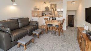 A modern living room with a brown leather sofa, a wooden dining table with two chairs, and a small wooden cabinet.