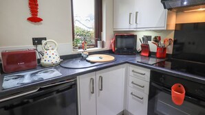 A modern kitchen with white cabinets, a Bosch dishwasher, a red Bosch toaster, a polka-dotted kettle, and a red lobster decoration on the wall. - Corner Cottage (Windermere)