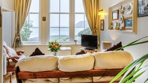 A living room with a sofa, TV, and a view of the sea through large windows. - Clooneavin Apartment 2 (Lynmouth)