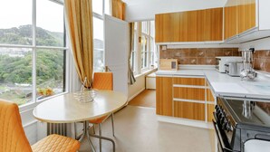 A modern kitchen with wooden cabinets, a stove, and a dining area with a table and chairs. - Clooneavin Apartment 2 (Lynmouth)