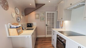 A compact kitchen with a white countertop, a built-in oven, and a wooden stool. - The Mounting Steps (Ambleside)