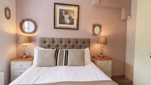 A neatly arranged bedroom with a tufted headboard, a framed deer artwork, two bedside lamps, and a white wardrobe. - The Mounting Steps (Ambleside)