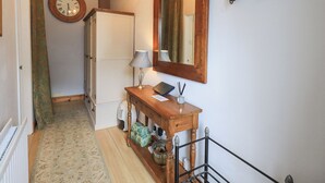A hallway with a wooden console table, a mirror, a clock, and a radiator. - The Mounting Steps (Ambleside)