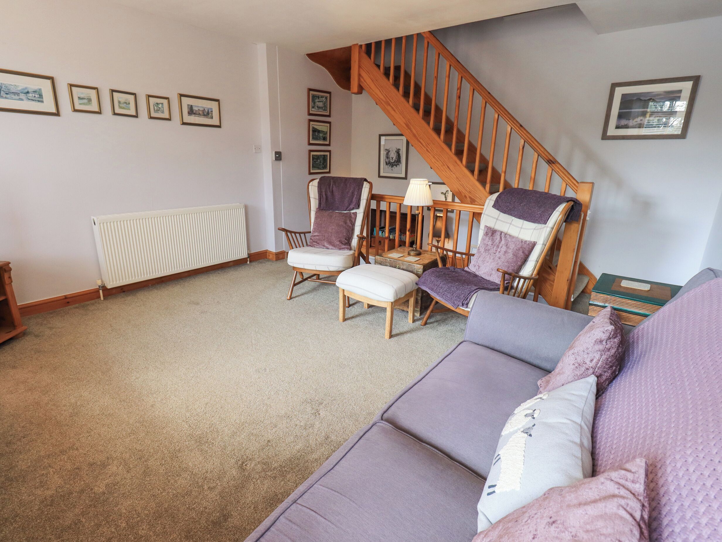 A living room with a wooden staircase, a white radiator, and a grey sofa with cushions.