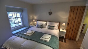 Une chambre à coucher comprenant un lit, deux tables de chevet, une fenêtre, un objet de décoration en forme de cœur et une armoire en bois.