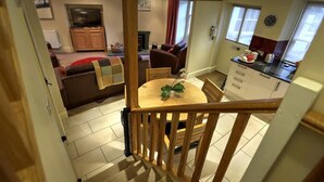 Un coin repas avec une table et des chaises en bois, une petite plante en pot, et une vue sur un salon avec un canapé et un téléviseur.