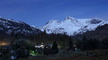 Un paisaje montañoso con picos nevados y un pequeño poblado con casas y una calle iluminada.