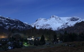 Un paisaje montañoso con picos nevados y un pequeño poblado con casas y una calle iluminada.