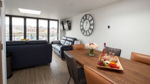 Een moderne woonkamer met een bank, een eettafel met een fruitschaal en een grote wandklok.