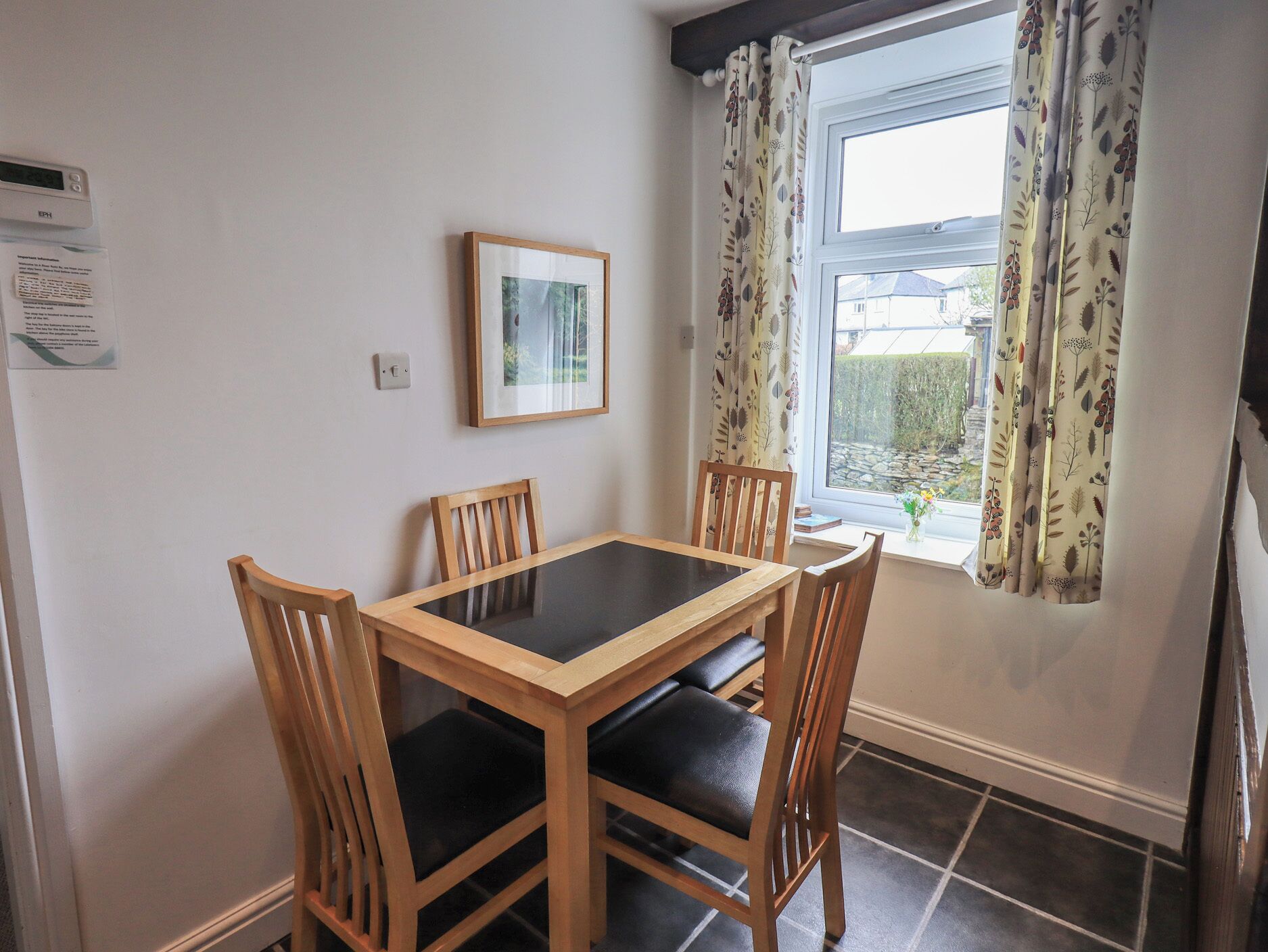 A dining area with a table and chairs, a framed picture on the wall, and a window with curtains.