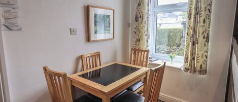 A dining area with a table and chairs, a framed picture on the wall, and a window with curtains.