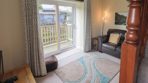 Un salon avec une porte-fenêtre coulissante donnant sur un balcon, un canapé en cuir, une table basse en bois et un tapis.