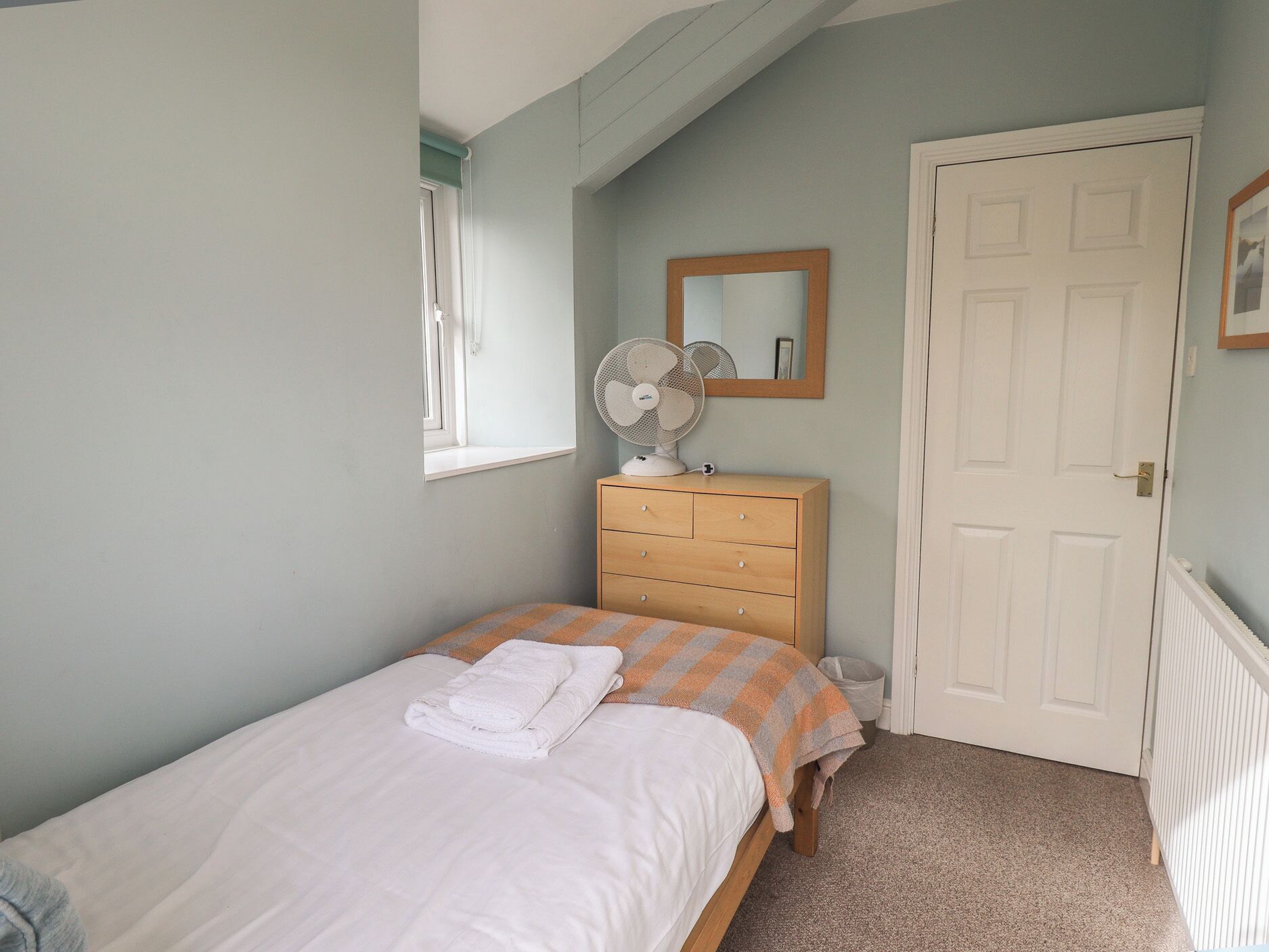 A bedroom with a bed, a dresser, a fan, a mirror, and a door.