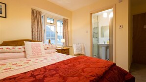 A bedroom with a large bed, a bedside table, a window with curtains, and a bathroom visible through an open door. - Grange Fell (Keswick)