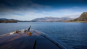 A boat deck with a metal railing and a wooden floor, overlooking a calm lake with mountains in the distance. - Grange Fell (Keswick)