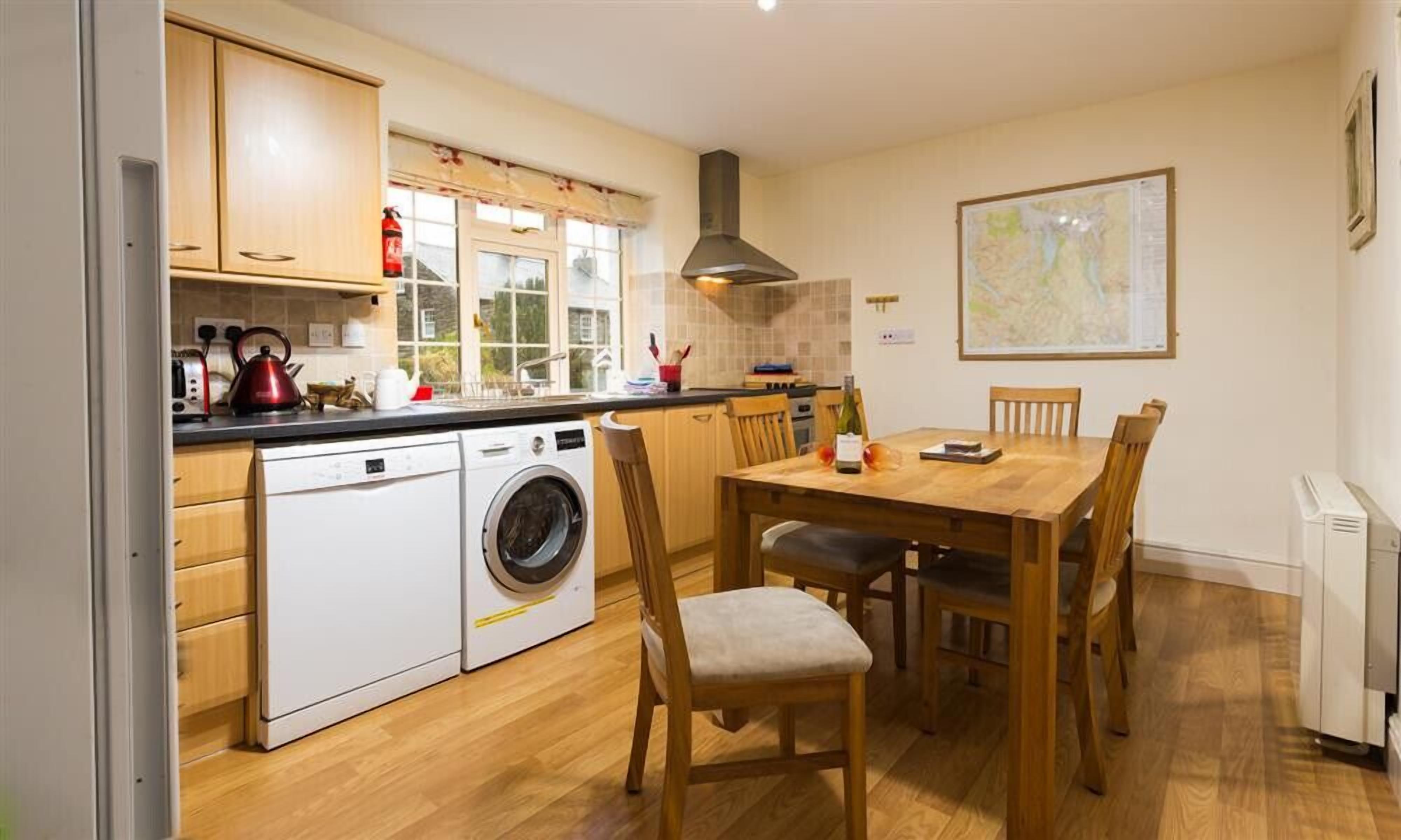 A compact kitchen with a washing machine, wooden cabinets, a dining table with chairs, and a map on the wall.