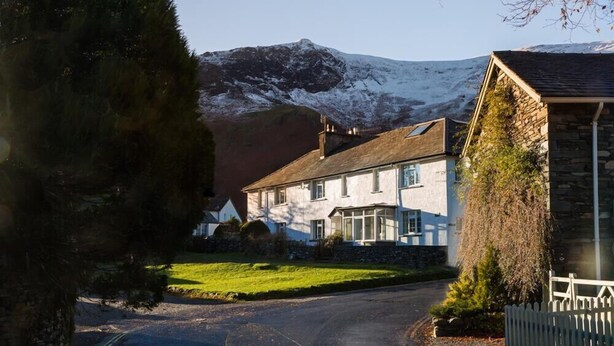 A two-story house with a stone facade, a visible chimney, and a grassy yard. - Grange Fell (Keswick)