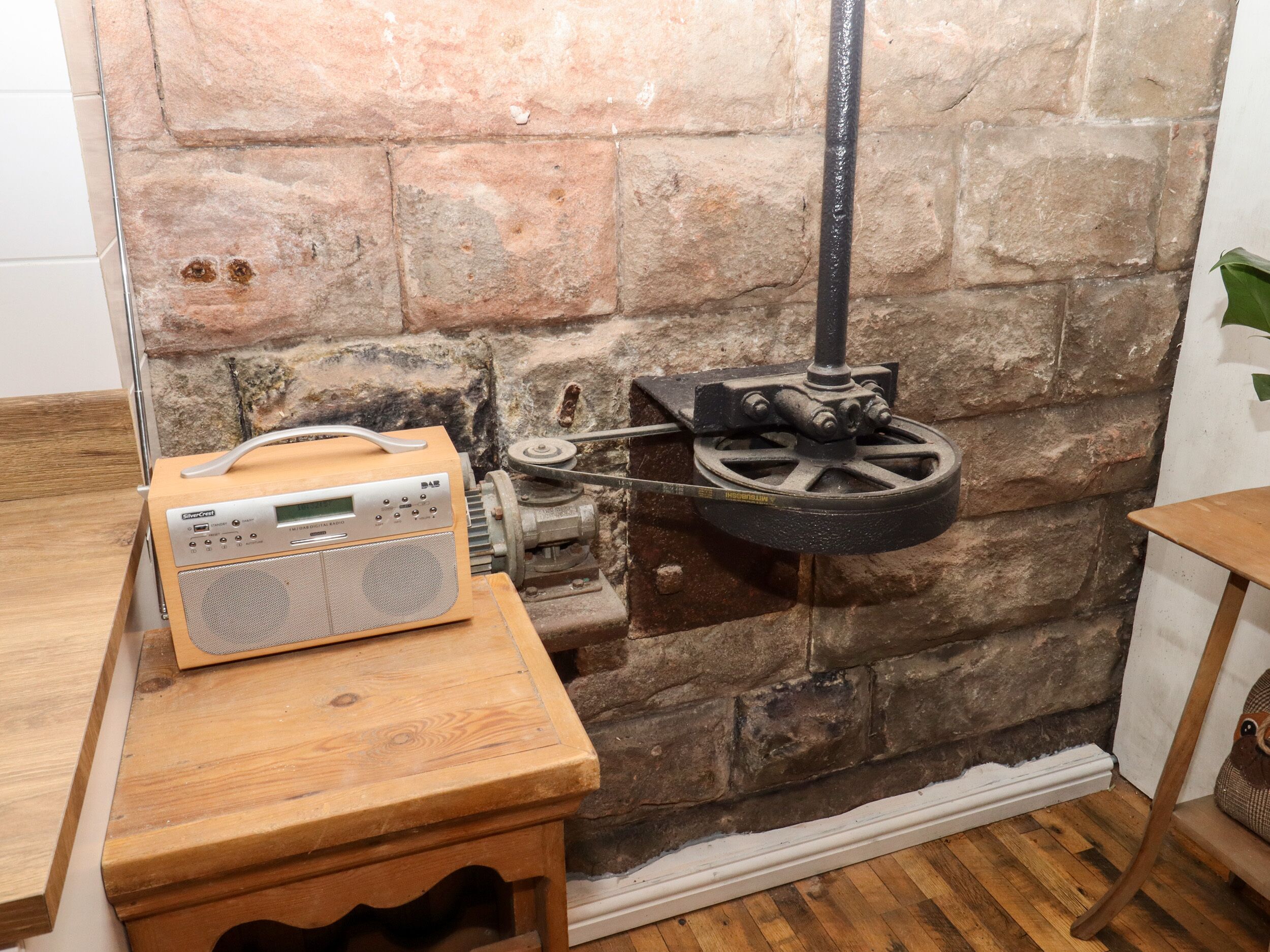 Quarto rústico com parede de pedra, uma mesa de madeira com um rádio e um mecanismo de roda de metal.