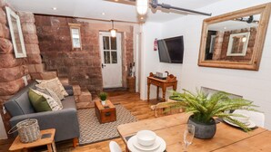 Ein gemütliches Wohnzimmer mit Steinwand, einer Couch, einem Couchtisch, einem Esstisch mit Stühlen, einem Fernseher und einem Kamin.