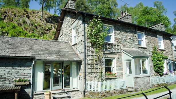 A stone building with a sloped roof, large windows, and a white picket fence. - Oakbank (Ambleside)