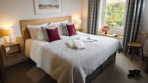 A neatly made bed with white and grey bedding, a wooden headboard, and a window with curtains. - Oakbank (Ambleside)