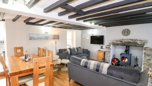 A cozy living room with a sofa, wooden dining table, and a stone fireplace. - Min-y-rhos (Pwllheli)