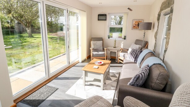 A spacious living room with a large sliding glass door leading to a garden, a sofa set, a small table, and a lamp. - Min-y-rhos (Pwllheli)