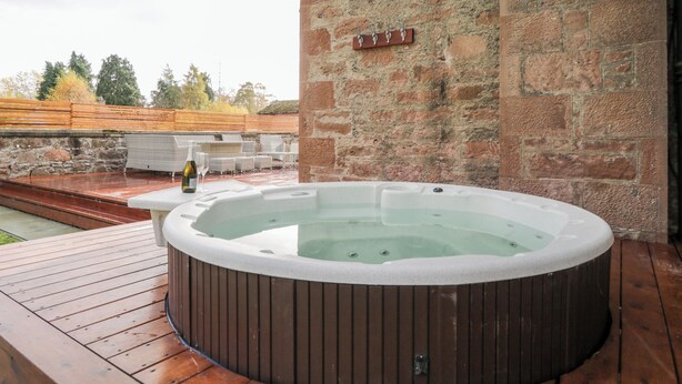 A hot tub on a wooden deck with a stone wall backdrop.