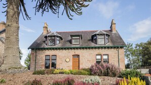 A stone house with a green roof, two dormer windows, and a wooden door.