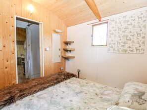 A wooden-paneled room with a bed, a mirror, a window with a nature-themed curtain, and a wall-mounted shelf. - Hugatree (King's Lynn)