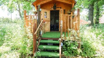 A wooden cabin with a green roof, a door, and a small porch area.