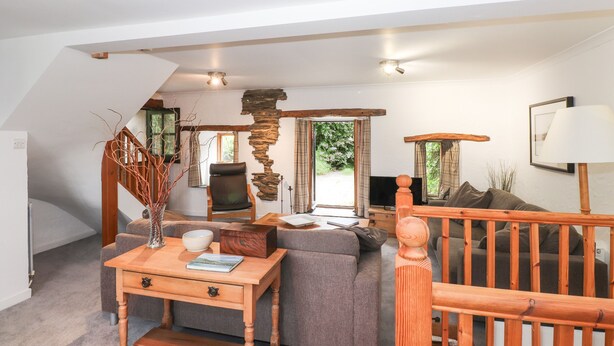 A cozy living room with a sofa, a wooden coffee table, a TV, and a stone accent wall. - Cherry Tree Cottage at Satterthwaite (Ulverston)