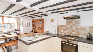 A kitchen with white cabinets, a wooden dining table, a hanging pot rack, and a tiled backsplash. - Cherry Tree Cottage at Satterthwaite (Ulverston)