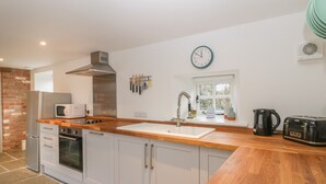 Une cuisine moderne avec des armoires blanches, un plan de travail en bois, un four encastré, un micro-ondes, un évier et une horloge murale.